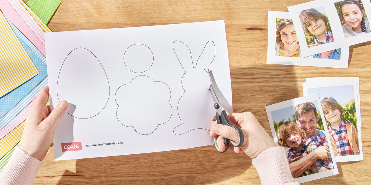 Dvě ruce vystřihly ze šablony velikonočního zajíčka. Vpravo od něj jsou vytištěny okamžité fotografie rodiny, vlevo jsou různé listy papíru.